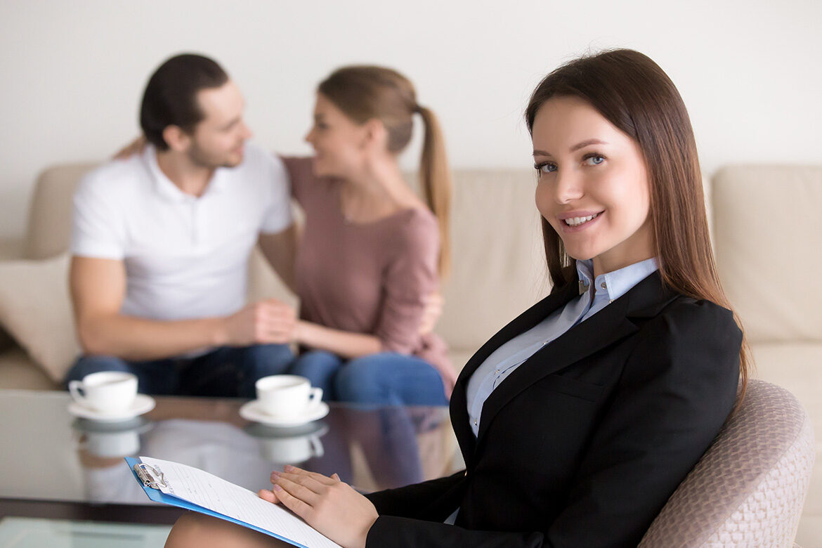 A professional woman smiles while a couple talks in the background.
