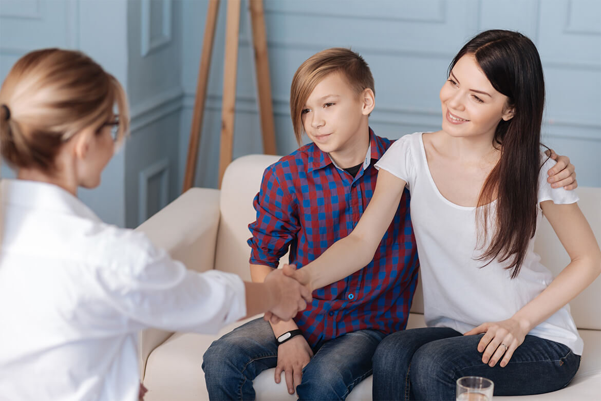 Mother and son shaking hands with a doctor during a consultation.