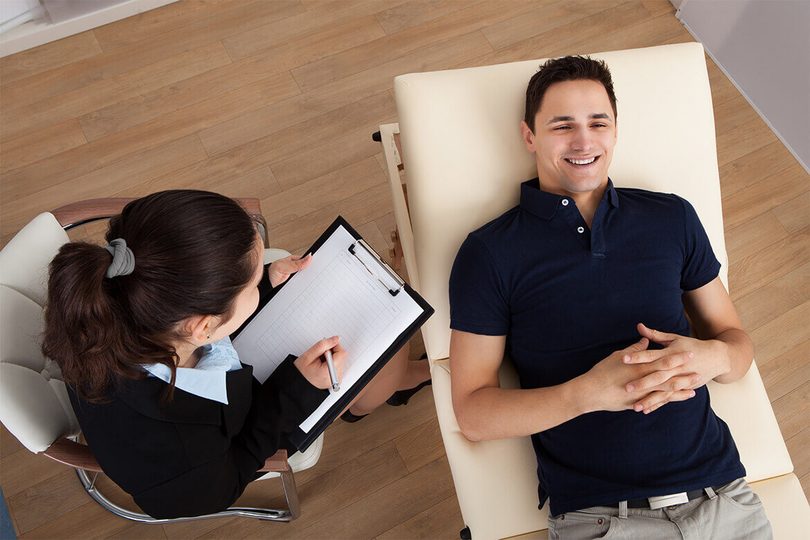 Man lying on a couch talking to a therapist taking notes.